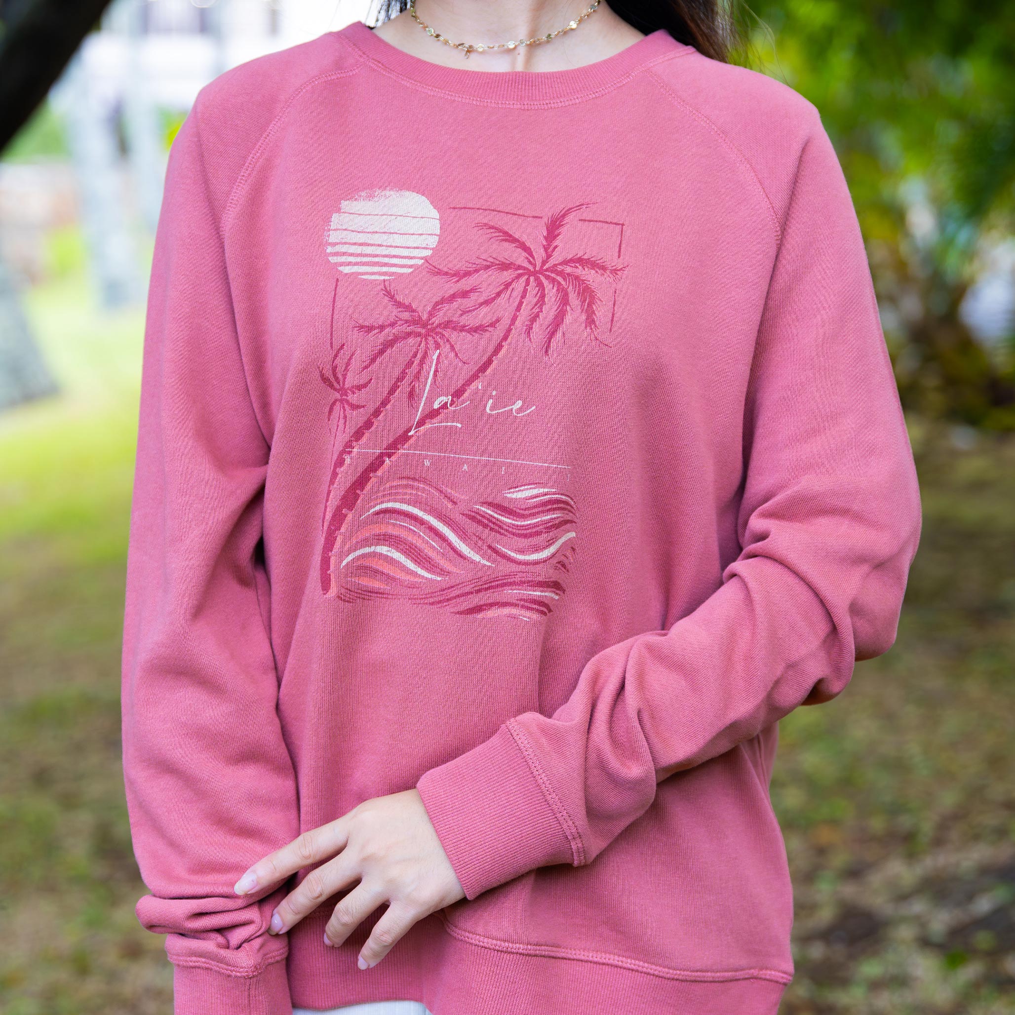 Person wearing a rose sweatshirt with palm tree and ocean wave design.