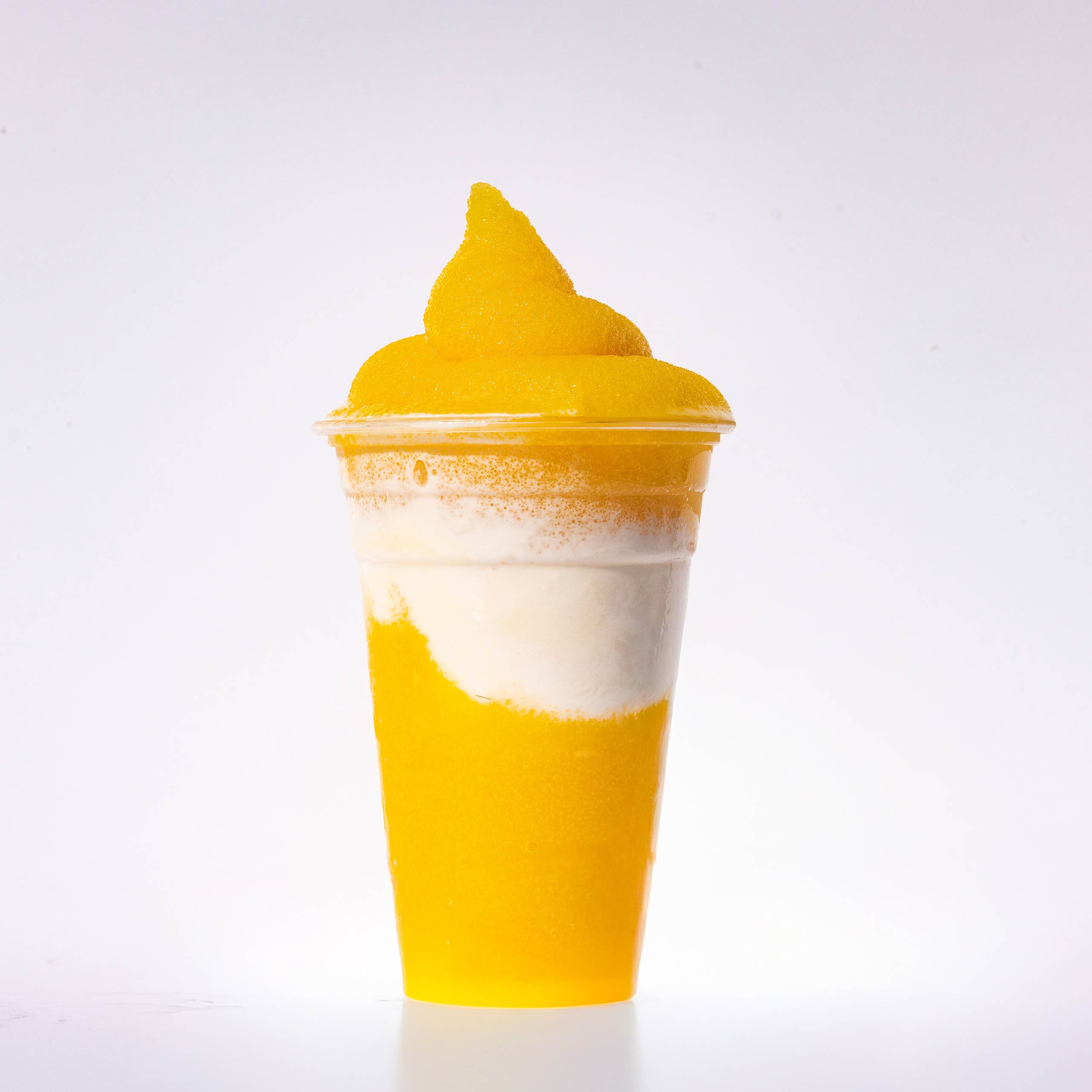 A layered yellow mango slushie swirled with a white creamy layer and a soft-serve peak on top.