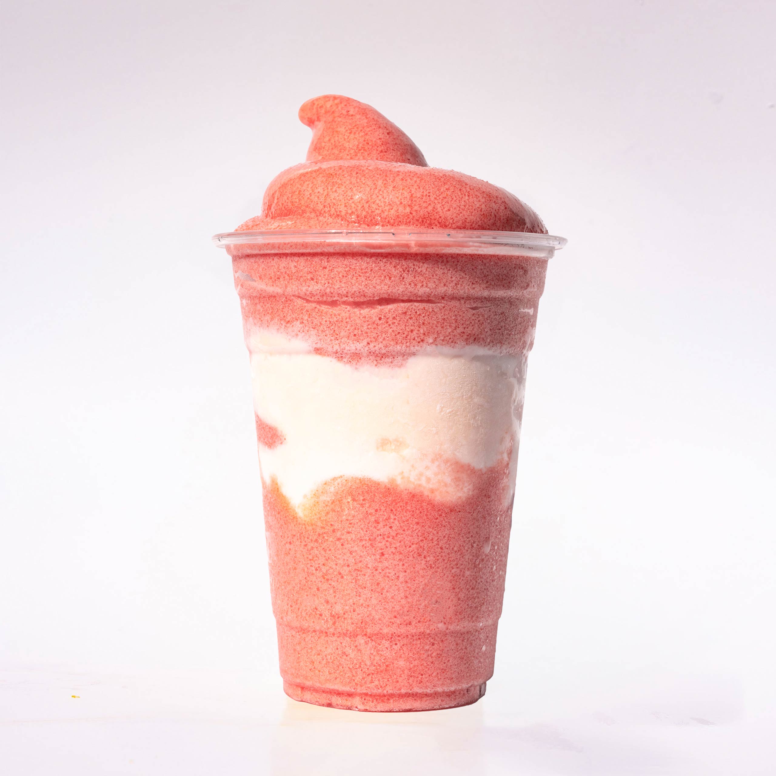 A layered pink and white slushie in a clear plastic cup with a soft-serve style swirl on top.