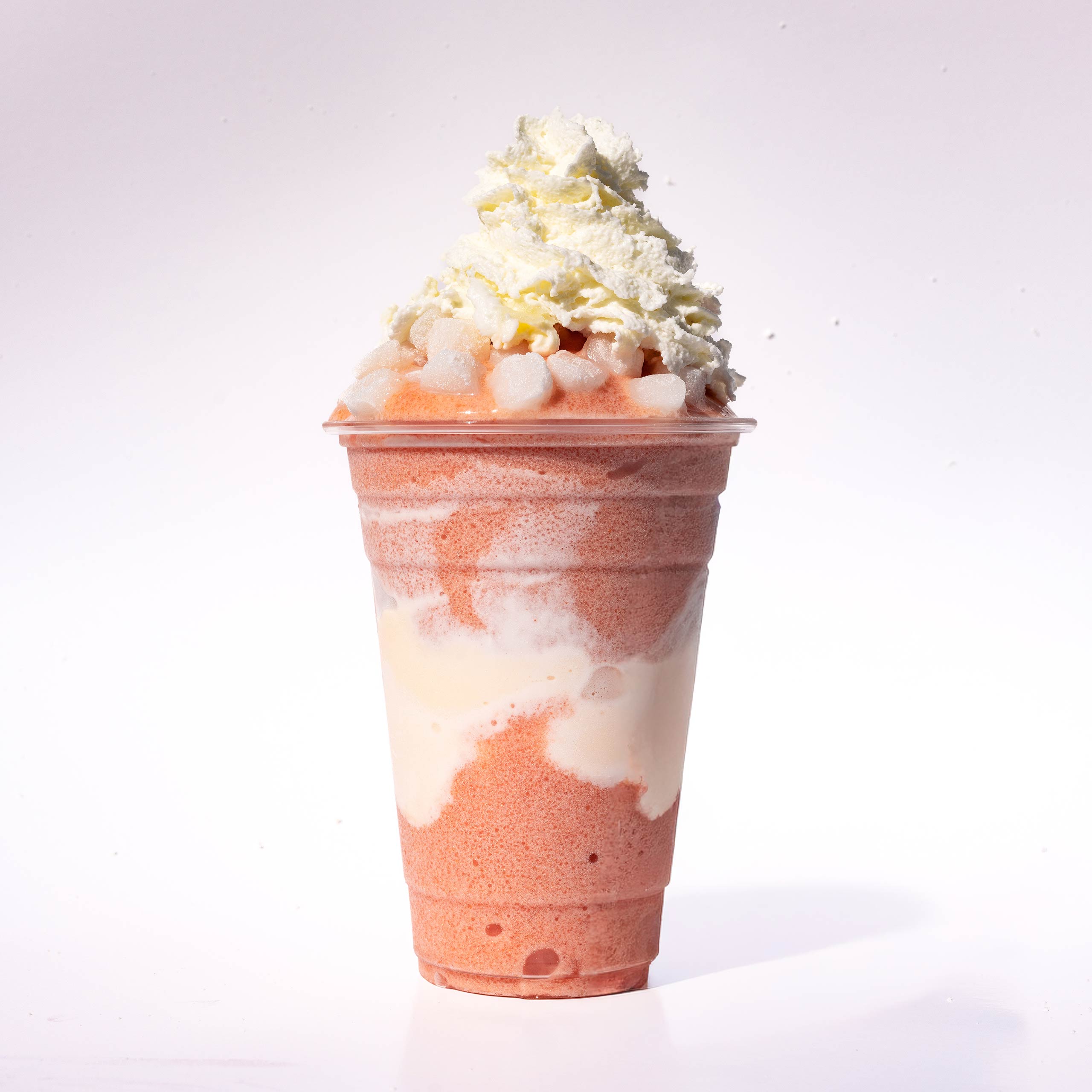 A layered pink and cream slushie topped with small mochi cubes and a large swirl of whipped cream.