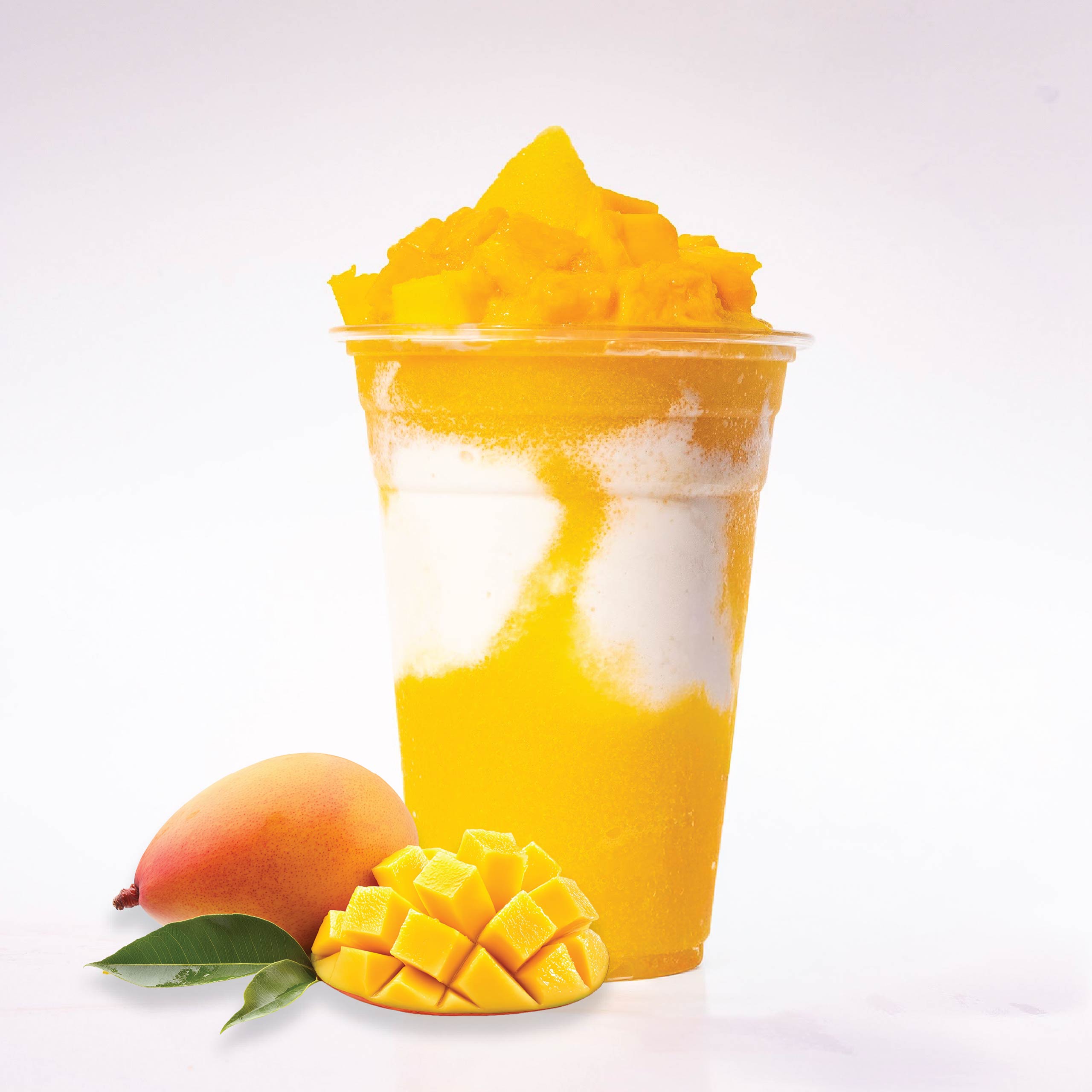 A layered mango slushie with chunks of fresh mango on top, sitting next to a whole and a sliced mango.