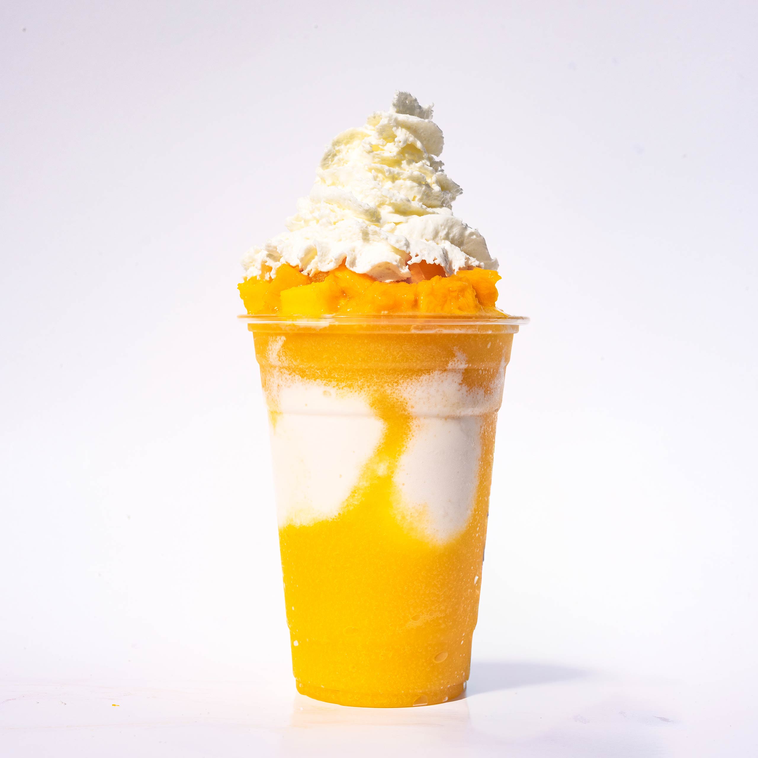 A layered mango and cream slushie topped with mango chunks and a generous swirl of whipped cream.